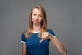 Beautiful young female with blonde straight hair looking is upset at the camera, holding thumb down. Concept of dislike Royalty Free Stock Photo