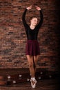 Beautiful young female classical ballet dancer on pointe shoes wearing a black leotard and skirt on a brick background