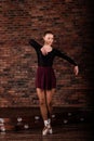 Beautiful young female classical ballet dancer on pointe shoes wearing a black leotard and skirt on a brick background