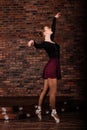 Beautiful young female classical ballet dancer on pointe shoes wearing a black leotard and skirt on a brick background