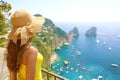 Beautiful young female model with straw hat in Capri Island with Faraglioni sea stack and blue crystalline water on the background