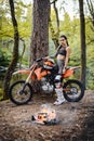 Beautiful young female racer wearing motocross outfit with semi naked torso sitting on her bike next to the bonfire in Royalty Free Stock Photo