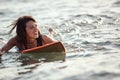 Beautiful young female surfer swimming on surfboard, smiling. copy space