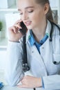 Beautiful young female therapeutist doctor sitting in front of working table with laptop and documents on it and calling Royalty Free Stock Photo