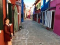 A beautiful young female tourist posing along a narrow brick road full of old colourful homes and flowers in Burano, Italy Royalty Free Stock Photo