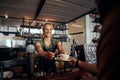 Beautiful young female waiter serving cup of coffee to customer in modern cafe Royalty Free Stock Photo