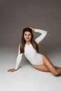 Beautiful young fit girl in white bodysuit, tanned slim female model with long healthy hairs posing on studio floor Royalty Free Stock Photo