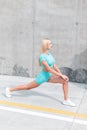 Beautiful young fitness model girl in fashion blue sportswear starts jogging and stretches near a gray wall on the street