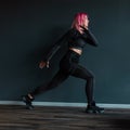 Beautiful young fitness woman in black sportswear with sneakers starts workout near a black wall in the gym