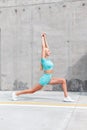 Beautiful young fitness woman with slender sexy body in blue sportswear with white shoes doing stretching near gray wall in the Royalty Free Stock Photo