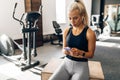 Young fitness woman, in sportswear, relaxing after a workout uses a mobile phone, in the gym