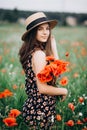 Beautiful young free girl in a hat in a summer field of red poppies with a bouquet. Soft selective focus