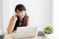 Beautiful young freelance asian woman smiling working on laptop computer and talking mobile smart phone Royalty Free Stock Photo