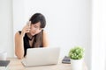 Beautiful young freelance asian woman smiling working on laptop computer and talking mobile smart phone at desk Royalty Free Stock Photo