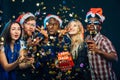 Friends at New Year`s party, wearing santa hats, dancing and blowing confetti Royalty Free Stock Photo