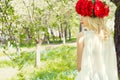 Beautiful young gentle elegant young blond woman with red peony in a wreath of white blouse walking in the lush apple orchard