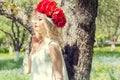 Beautiful young gentle elegant young blond woman with red peony in a wreath of white blouse walking in the lush apple orchard