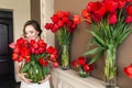 A beautiful young girl in a bathrobe holds in her hands a lot of red tulips in a vase. March 8 concept. Royalty Free Stock Photo