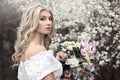 Beautiful young girl in a beautiful white dress with a bouquet near a flowering tree. Royalty Free Stock Photo