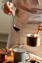 Beautiful young girl in beige apron is preparing delicious organic hot chocolate in old vintage ladle. Soft daylight, lifestyle Royalty Free Stock Photo