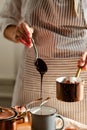 Beautiful young girl in beige apron is preparing delicious organic hot chocolate in old vintage ladle. Soft daylight, lifestyle Royalty Free Stock Photo