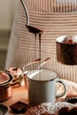 Beautiful young girl in beige apron is preparing delicious organic hot chocolate in old vintage ladle. Soft daylight, lifestyle Royalty Free Stock Photo