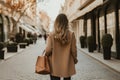 Beautiful young girl in a beige coat with a brown handbag walks along the street. A stylish Womens rear view walking with a