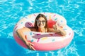 Beautiful young girl in bikini with donut inflatable pink circle in blue swimming pool