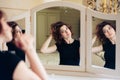 Beautiful young girl in a black dress sits in front of a vintage mirror, reflected in three mirrors