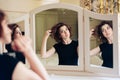 Beautiful young girl in a black dress sits in front of a vintage mirror, reflected in three mirrors