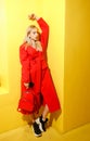 Beautiful young girl blogger dressed in stylish red coat poses on the background of yellow walls in the show room