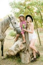 Beautiful young girl with blond hair in a suede jacket with fringe with little sister in a straw hat and checkered vintage dress Royalty Free Stock Photo