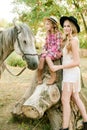 Beautiful young girl with blond hair in a suede jacket with fringe with little sister in a straw hat and checkered vintage dress Royalty Free Stock Photo