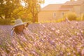 The beautiful young girl in a blue dress and cap sits in a lavender flowers, long curly hair, smile, pleasure, a house