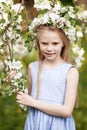 Beautiful young girl in blue dress in the garden with blosoming apple trees. Cute girl holding apple-tree branch