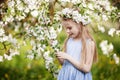 Beautiful young girl in blue dress in the garden with blosoming apple trees. Cute girl holding apple-tree branch