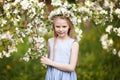 Beautiful young girl in blue dress in the garden with blosoming apple trees. Cute girl holding apple-tree branch