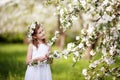 Beautiful young girl in blue dress in the garden with blosoming apple trees. Cute girl holding apple-tree branch
