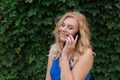 Beautiful young girl in a blue dress talking on the phone. Against the background of wild grapes, summer day. Copy space Royalty Free Stock Photo