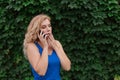 Beautiful young girl in a blue dress talking on the phone. Against the background of wild grapes, summer day. Copy space Royalty Free Stock Photo