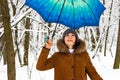 Beautiful young girl with blue umbrella in snowy forest. Snowfall concept. Woman under wet snow rain in winter park.