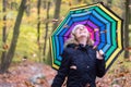 Beautiful young girl with colorful umbrella is enjoying the dropping leaves in the autumnal forest