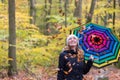 Beautiful young girl with colorful umbrella is enjoying the dropping leaves in the autumnal forest