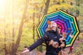 Beautiful young girl with colorful umbrella is enjoying the dropping leaves in the autumnal forest