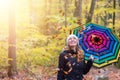 Beautiful young girl with colorful umbrella is enjoying the dropping leaves in the autumnal forest