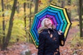 Beautiful young girl with colorful umbrella is enjoying the dropping leaves in the autumnal forest