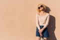 Beautiful young girl with curls in sunglasses stands near the wall in sunlight at sunset