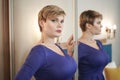 The beautiful young girl with curvy figure and short hair in fashion dress near the mirror