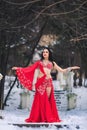 Beautiful young girl dancing belly dance in red dress in winter in a park on the snow. Royalty Free Stock Photo