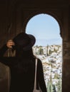 A beautiful young girl in a dress and a hat looking at the Albaicin district of Granada from the window of the Alhambra palace Royalty Free Stock Photo